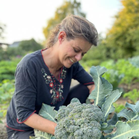 Billedet forestiller en smilende kvinde, der høster en broccoli