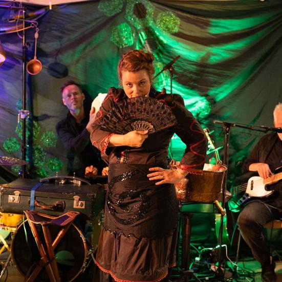 Billedet viser en kvinde med en vifte foran to musikere