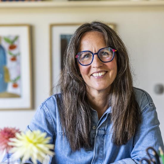 Billedet viser en smilende Puk Hyllested ved et bord med en kop kaffe og en journal
