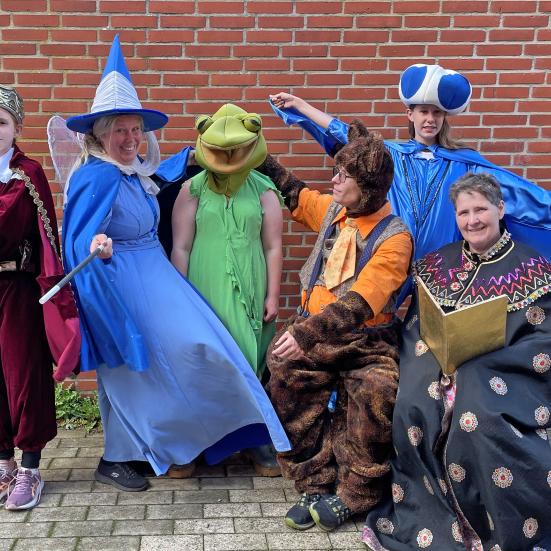Billedet viser seks udklædte mennesker foran en rød mur