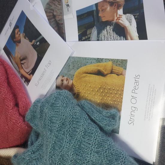 Fotoet viser strikketøj, som ligger oven på forskellige strikkeopskrifter