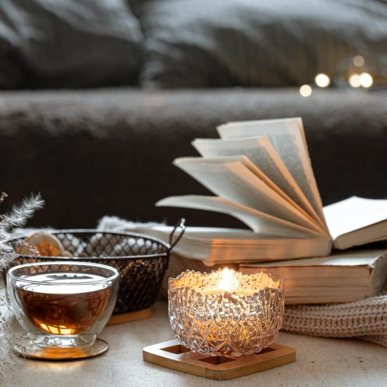 Fotoet viser en opslået bog på et sofabord med stearinlys, te og et lunt tæppe