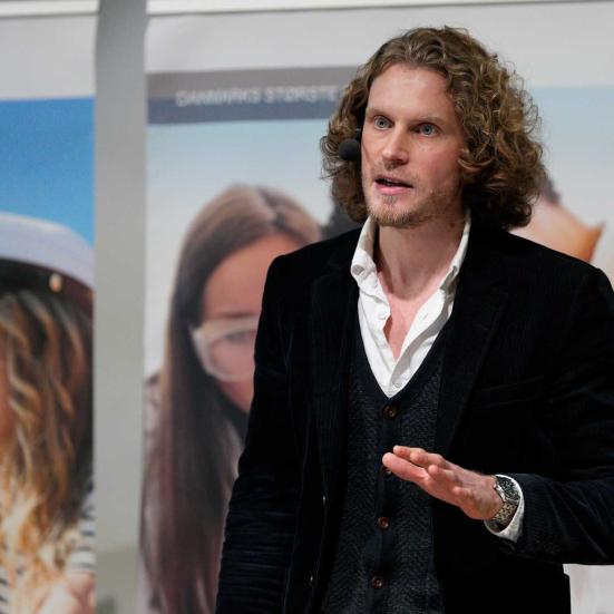 Fotoet viser Joachim Meier midt i en tale foran plancher med billeder af unge studenter