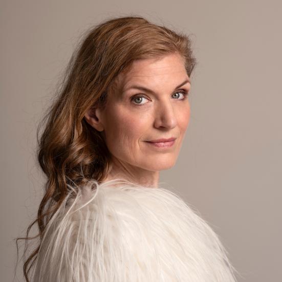 Fotoet viser Iben Mondrup foran en grå væg. Hun står med siden til og smiler svagt mod kameraet