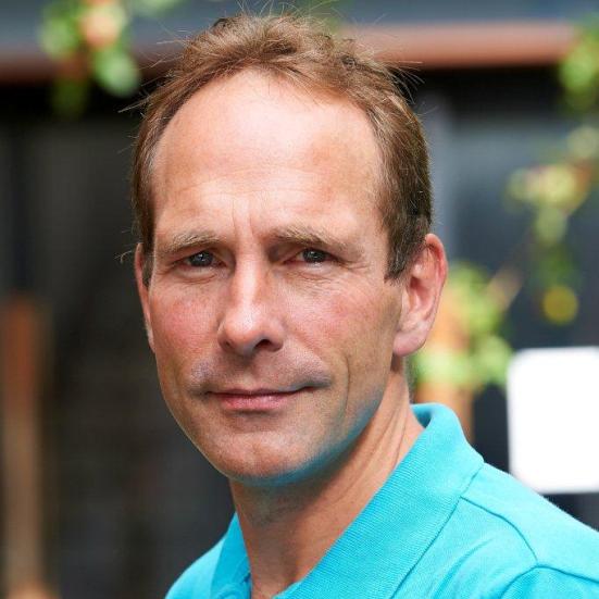 Fotoet viser Peter Viggo Jakobsen, som ser direkte ind i kameraet iført en turkis poloshirt foran en sløret baggrund