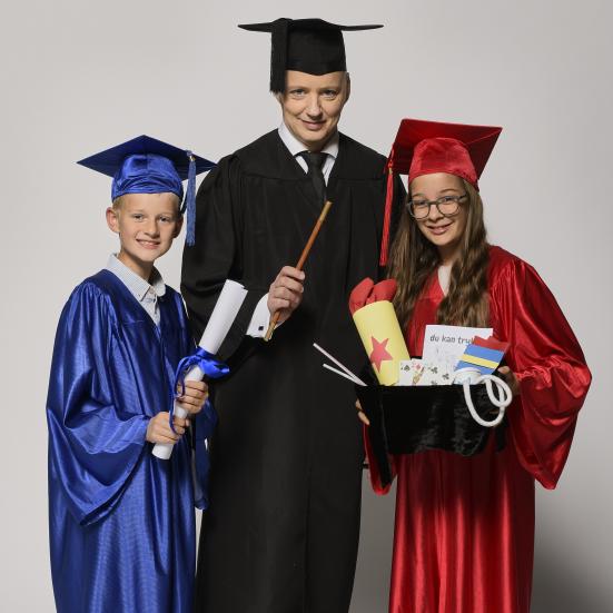 Fotoet viser en voksen og to børn iført skinnende kåber, hatte med kvast, tryllestav og trylleremedier