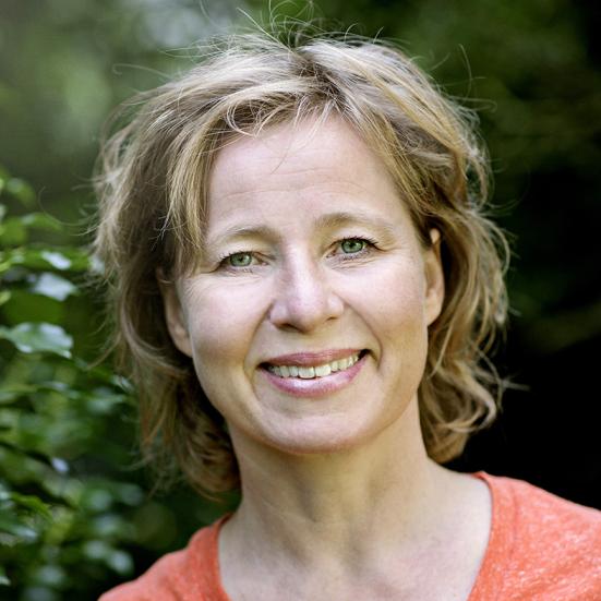 Billedet viser en smilende Anette Sams foran en grøn busk