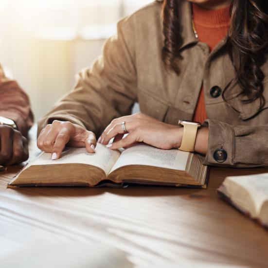 Billedet viser tre opslåede bøger på et bord, samt hænderne på dem, der sidder med bøgerne