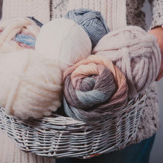 Billedet forestiller en kvinde som holder en kurv fyldt med garnnøgler.