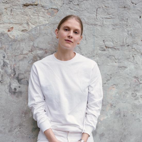Billedet viser Emma Holten i hvidt tøj foran en slidt mur