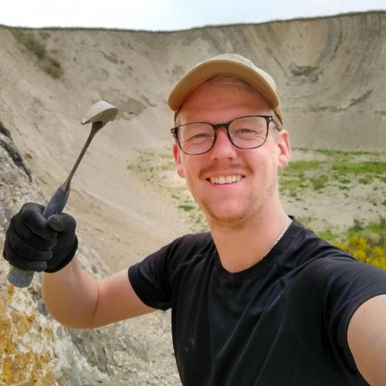 Billedet viser en smilende mand med en fossilhammer i hånden