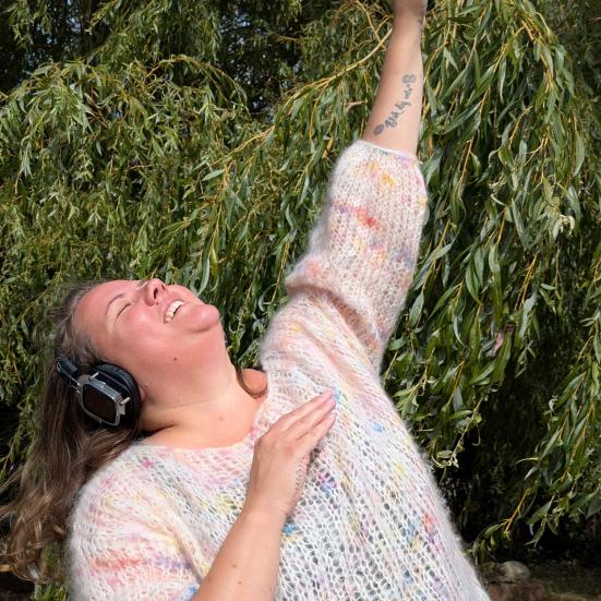Kvinde har høretelefoner på og danser foran grønne træer.