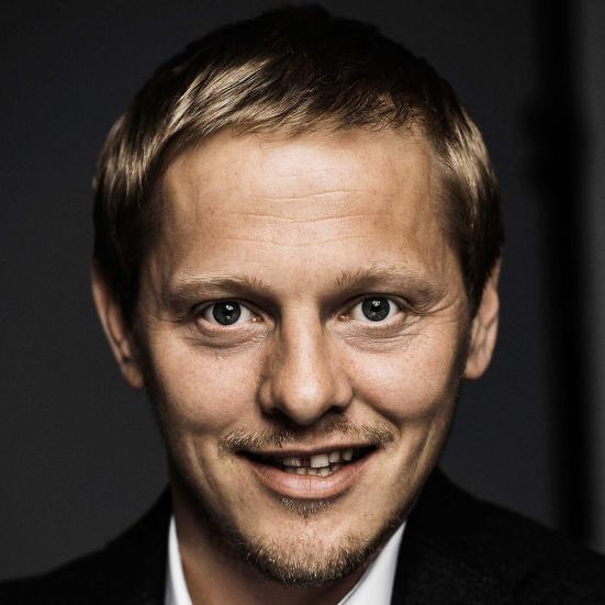 Billedet er et nærfoto af Thure Lindhart, som smiler og ser direkte ind i linsen