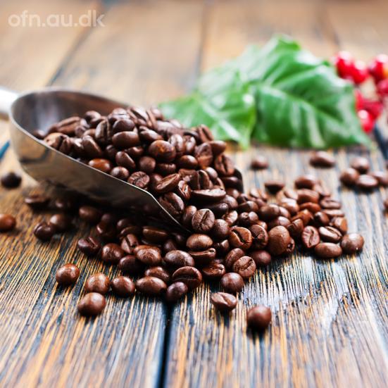 Billedet viser en måleske med kaffebønner på et plankebord