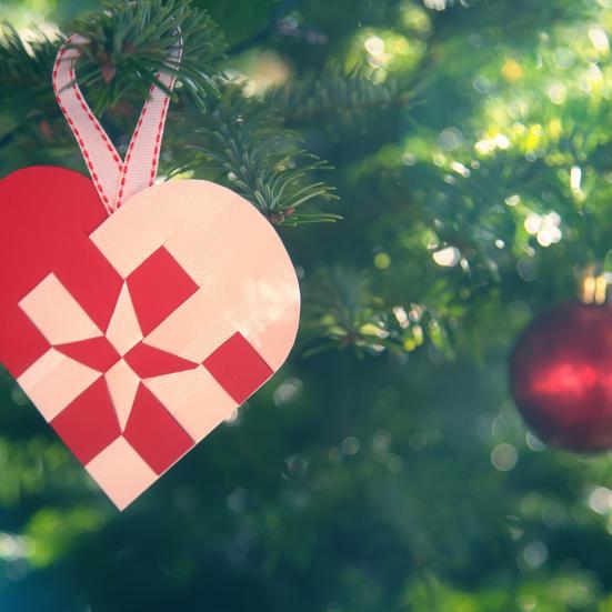 Billedet viser et flettet julehjerte og en rød julekugle på et juletræ