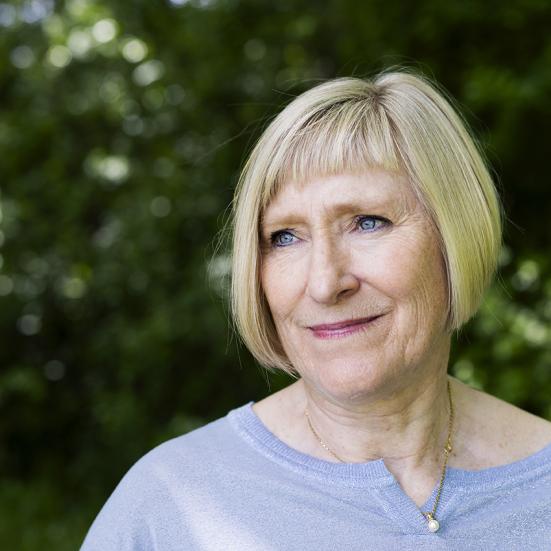 Billedet viser en smilende Pernille Juhl foran et grønt buskads