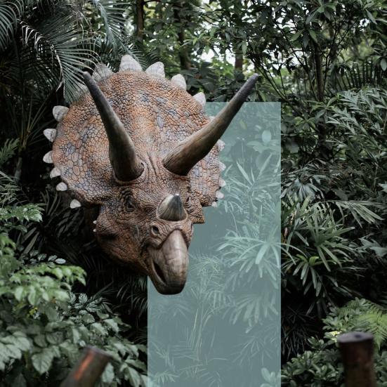 En hornet dinosaur stikker hovedet frem mellem tæt, grøn jungle.