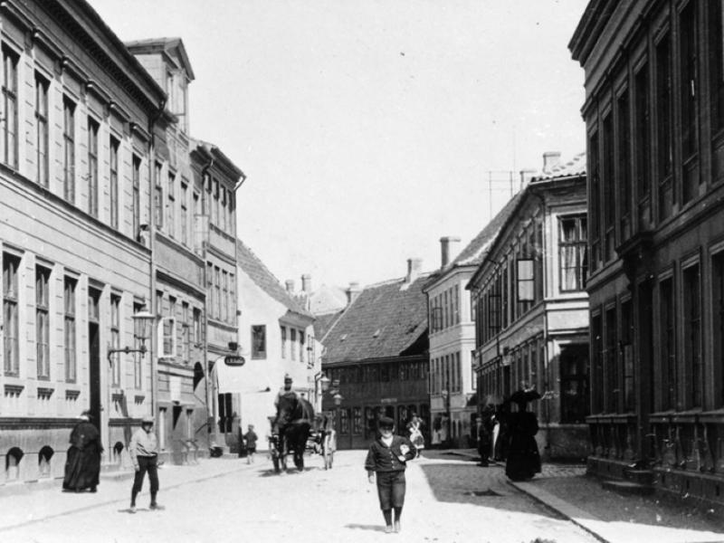 Billedet er i sorthvid og forestiller en gade med rækker af bygninger på begge sider.