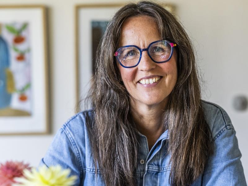 Billedet viser en smilende Puk Hyllested ved et bord med en kop kaffe og en journal