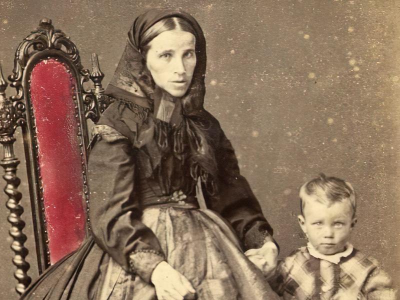 Billedet er et gammelt, sort/hvid foto af en kvinde med et lille barn