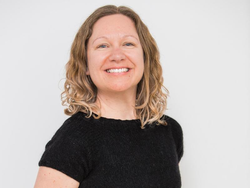 Fotoet viser en smilende Jane Ibsen Piper i en sort T-shirt foran en hvid væg