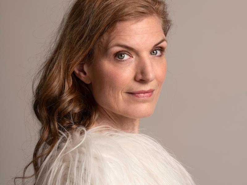 Fotoet viser Iben Mondrup foran en grå væg. Hun står med siden til og smiler svagt mod kameraet