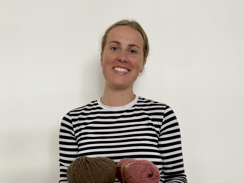 Fotoet viser en smilende Johanne Bisgaard med en stak bøger og et par garnnøgler i favnen