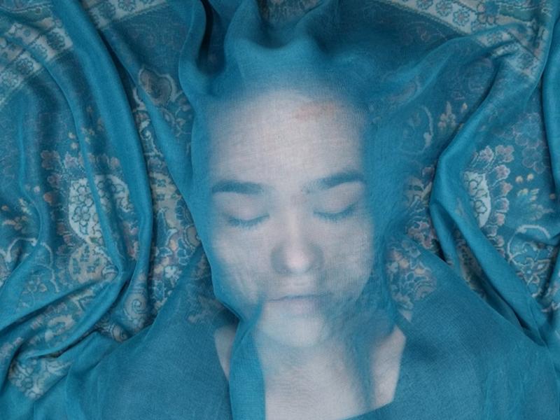 Billedet forestiller en kvinde liggende under et gennemsigtig sjal i en blålig farve.