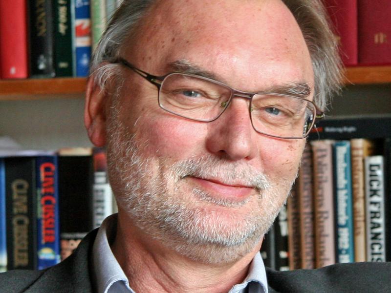 Billedet viser en smilende Leif Davidsen foran en bogreol