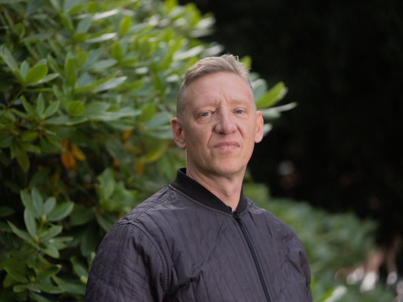 Billedet viser Christian Groes foran en grøn rhododendron