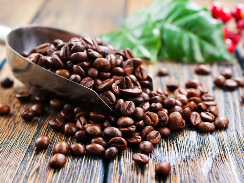 Billedet viser en måleske med kaffebønner på et plankebord