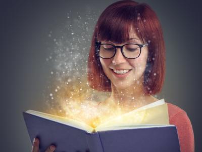 Billedet forestiller en ung kvinde med briller. Hun ser smilende ned på en opslået bog. Et gyldent lys vælder op fra bogens sider.