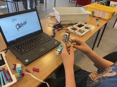 Billedet viser et par hænder, der er i gang med bygge en lego-figur foran en bærbar computer