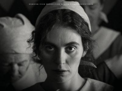 Billedet viser en sort/hvid filmplakat for Pigen med nålen med en ung kvinde i forgrunden