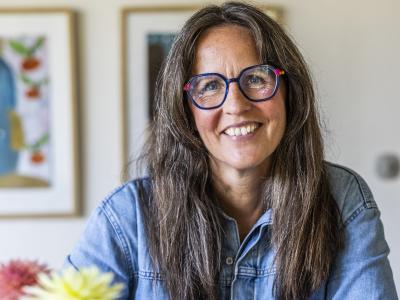 Billedet viser en smilende Puk Hyllested ved et bord med en kop kaffe og en journal