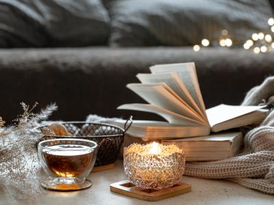 Fotoet viser en opslået bog på et sofabord med stearinlys, te og et lunt tæppe