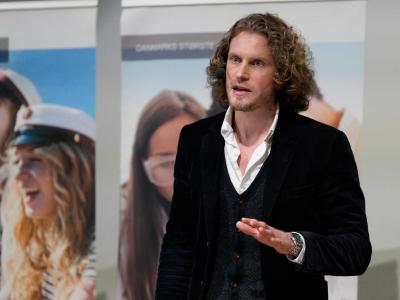 Fotoet viser Joachim Meier midt i en tale foran plancher med billeder af unge studenter