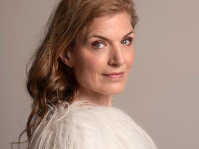 Fotoet viser Iben Mondrup foran en grå væg. Hun står med siden til og smiler svagt mod kameraet