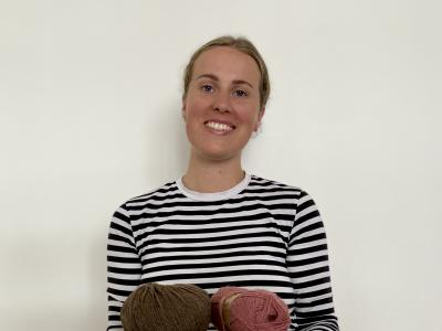 Fotoet viser en smilende Johanne Bisgaard med en stak bøger og et par garnnøgler i favnen