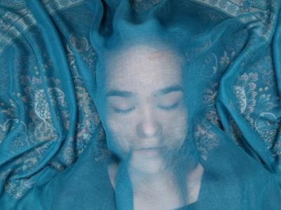 Billedet forestiller en kvinde liggende under et gennemsigtig sjal i en blålig farve.