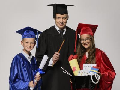 Fotoet viser en voksen og to børn iført skinnende kåber, hatte med kvast, tryllestav og trylleremedier