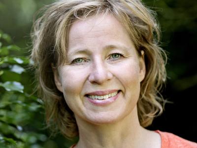 Billedet viser en smilende Anette Sams foran en grøn busk