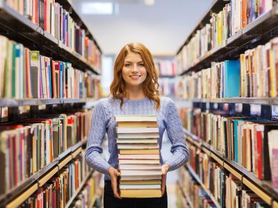 Billedet viser en kvinde med en stak bøger i hænderne mellem to store bogreoler