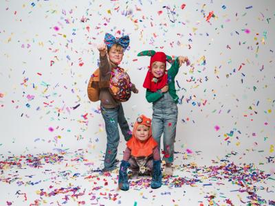 Billedet viser tre børn i en mængde farvestrålende konfetti