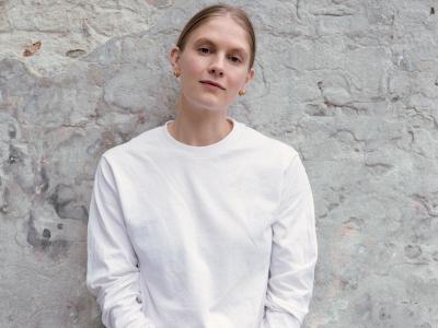 Billedet viser Emma Holten i hvidt tøj foran en slidt mur