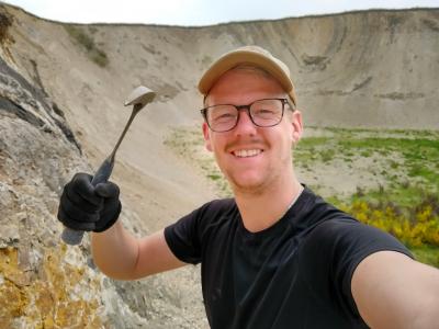 Billedet viser en smilende mand med en fossilhammer i hånden