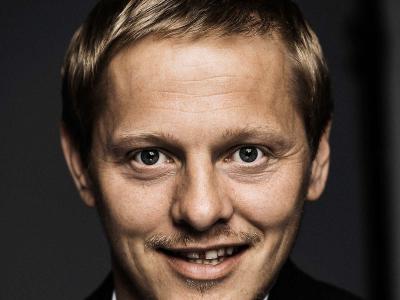 Billedet er et nærfoto af Thure Lindhart, som smiler og ser direkte ind i linsen
