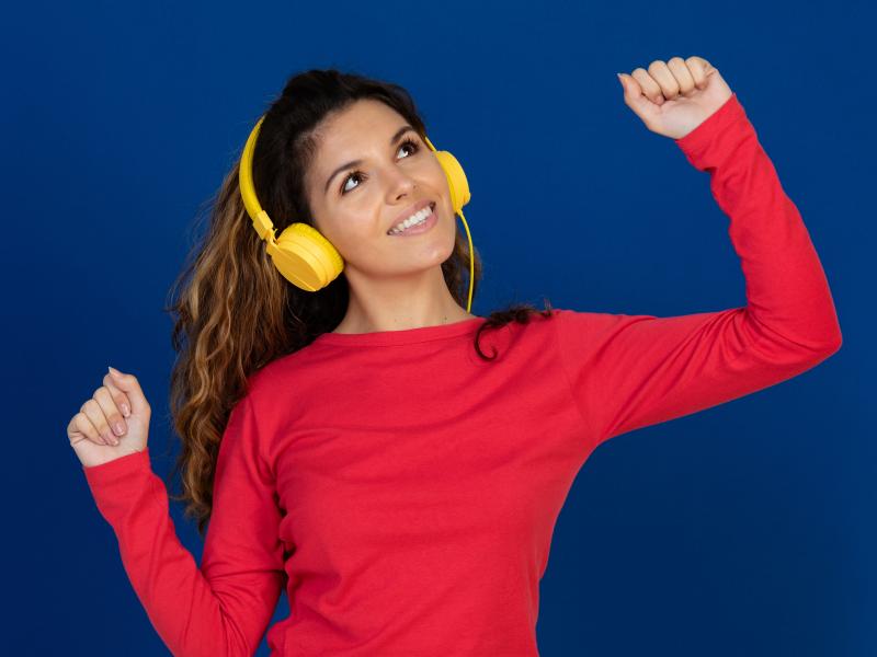 Billedet forestiller en kvinde i rød trøje der smiler og ser ud til at danse, mens hun lytter til musik.