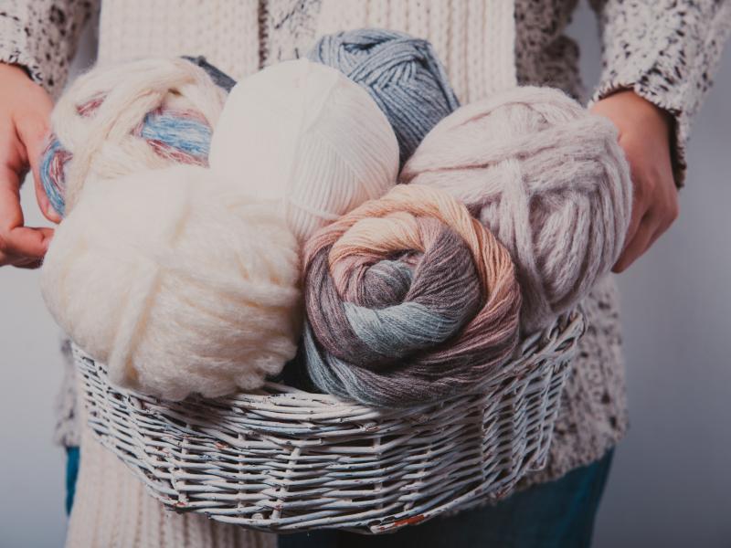 Billedet forestiller en kvinde som holder en kurv fyldt med garnnøgler.