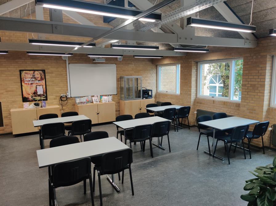 Billedet viser et område af Varde Bibliotek med fem borde og tilhørende stole